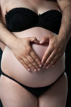 Cropped shot of man making shape of heart on wife&#039 s baby belly.
