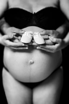 Shallow depth of field cropped shot of pregnant woman holding baby shoes with husband. Hands and belly only.