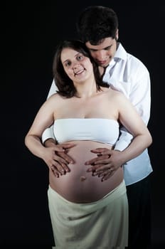 Portrait of happy young pregnant woman being hugged by husband.