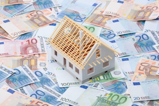 Building cost (construction cost) concept. Model of house under construction (rough construction) and money.