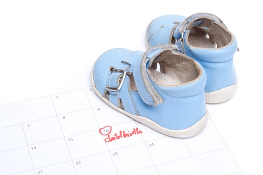 Handwritten text childbirth as reminder in calendar and baby shoes (bootee).