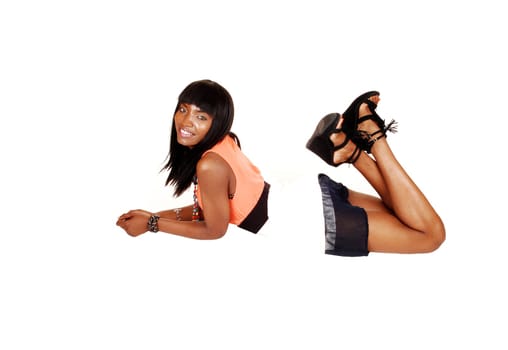 An afro American woman in a dress and heels lying on her stomach on the floor, looking into the camera, with her long black hair.