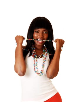 A young African American woman in a white top and long black hair standing for white background with her necklace in her mouths.