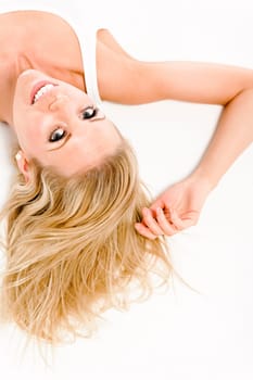 Attractive young woman in a white vest top sitting on the floor on white background