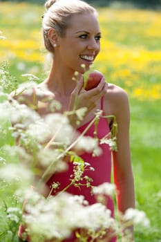 Beautiful young woman eating an apple on a summers day in the countryside.
