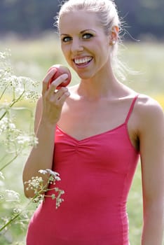 Beautiful young woman eating an apple on a summers day in the countryside.