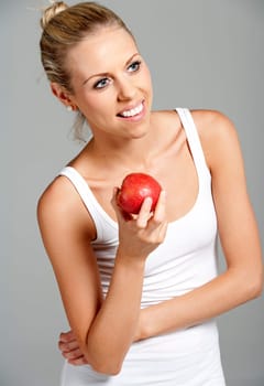 Beautiful young woman eating an apple wearing a white vest top