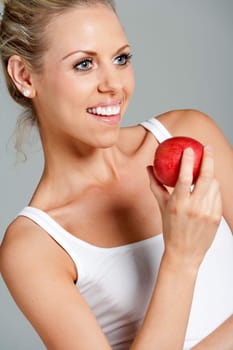 Beautiful young woman eating an apple wearing a white vest top