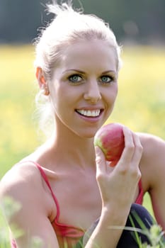 Beautiful young woman eating an apple on a summers day in the countryside.