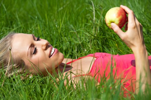 Beautiful young woman eating an apple on a summers day in the countryside.