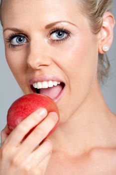 Beautiful young woman eating an apple wearing a white vest top