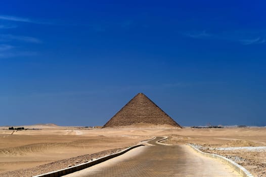 A row of camels transport tourists in front of all of the Dakshur Pyramids in Cairo, Egypt