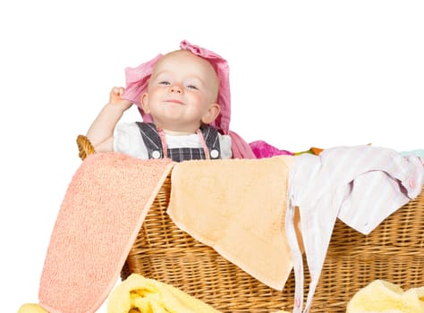 Impish little baby with a cute little self-satisfied expression sitting in amongst the washing in a wicker laundry basket