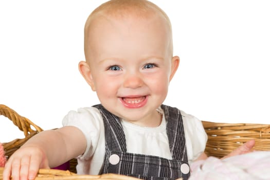 Adorable happy beaming baby with a wide toothy smile sitting in a wicker basket isolated on white