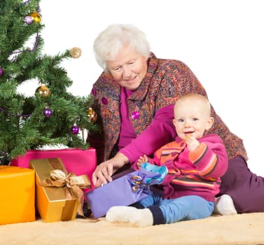Grandmother babysitting young baby sitting together on the floor alongside a decorated Christmas tree and giftwrapped presents