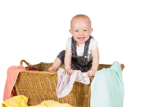 Joyful toddler witha lovely wide happy smile clambering out of a wicker basket with the laundry scattered around it
