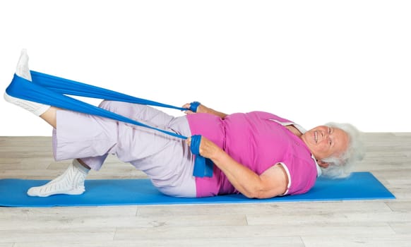 Overweight senior woman full of zest and vitality exercising on a gym mat with her leg raised in the air using a strap for leverage