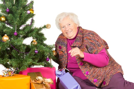 Happy senior lady and grandmother preparing for a family Christmas sitting decorating the Christmas tree and giftwrapped festive gifts