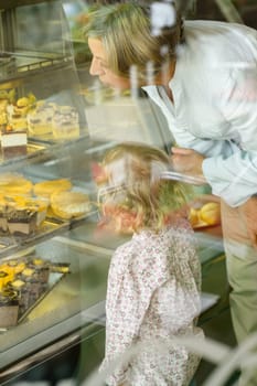 Grandchild and grandmother looking at cakes cafe window display dessert