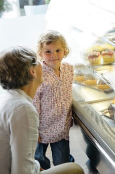Woman with child girl in bakery choose cake grandmother and granddaughter