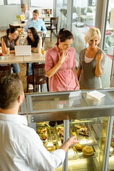 Waiter showing women cakes on window display cafe smiling friends