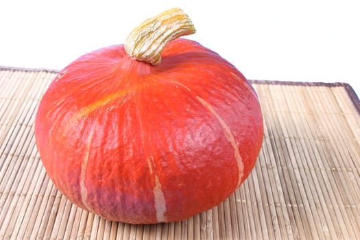 Hokkaido pumpkin (Cucurbita maxima) on a bamboo mat against a white background
