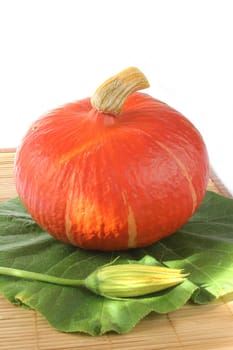 Hokkaido pumpkin (Cucurbita maxima) with leaf and flower on a bamboo mat against white background