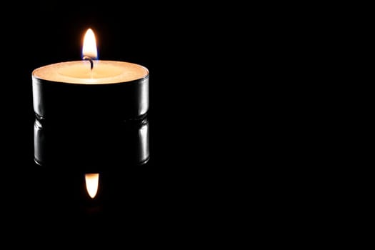 A tea light on a black reflective surface