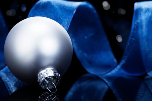 Silver Christmas bauble in front of blue ribbon on black background