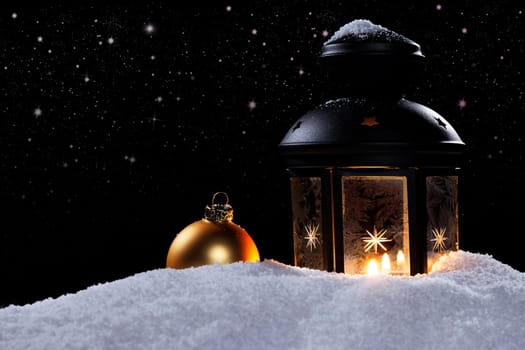 Lantern with Christmas bauble in the snow under starry sky