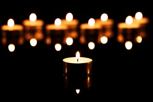 A tea light in front of many tea lights on black mirror