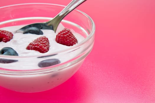 Bowl with jogurt and spoon on pink background
