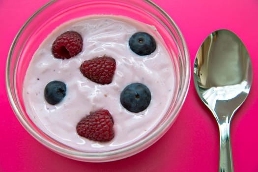 Jogurt has fixings of  fresh raspberries and blueberries