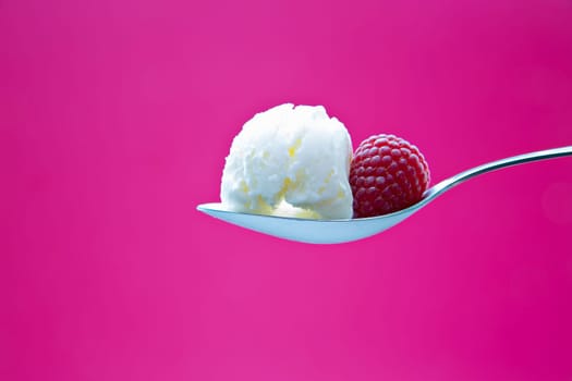 Tasty icecream on metal chromed spoon with raspberry
