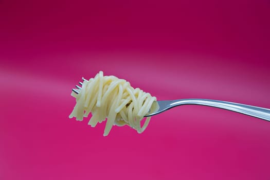 Tasty noodle on metal chromed fork on background