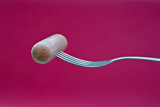 Round wiener on metal chromed fork on background