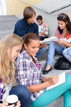 Students sitting on school steps writing studying teens college high-school