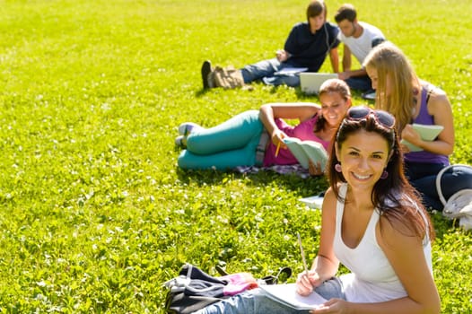 Students studying sitting on grass in park happy teens campus