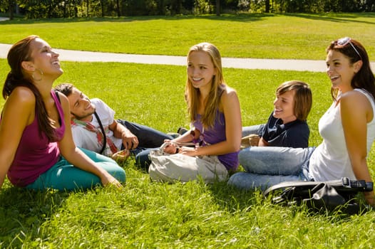 Teens sitting on lawn in park talking friends happy leisure