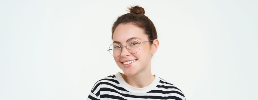 Image of young woman in glasses, using her mobile phone, standing with smartphone and smiling, standing over white background.