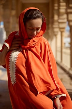 Authentic portrait of Middle Eastern pretty woman with head covered in hijab, dressed in traditional Moroccan Handora dress, posing against beige the mosque marble columns background. People. Religion
