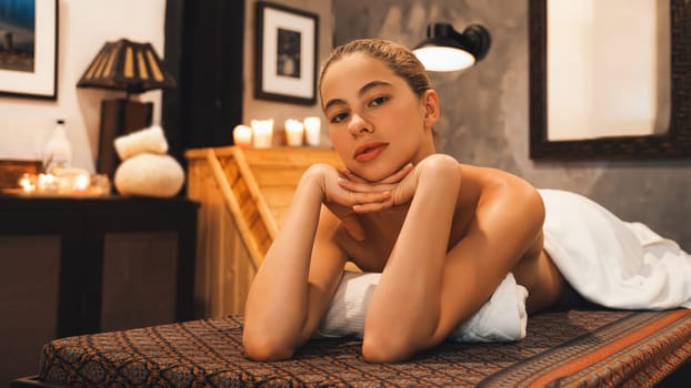 Portrait of beautiful caucasian woman in white towel woman lies on spa bed in front of warm wooden sauna cabinet with relaxation and peaceful at spa salon. Close up. A Side view. Tranquility.