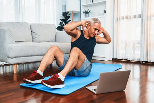 Athletic and sporty senior man doing crunch on the exercising mat while watching online exercising session at home exercise as concept of healthy fit body lifestyle after retirement. Clout