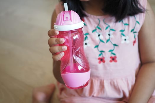 child girl drinking water sitting on sofa .