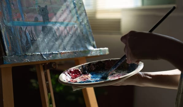 Close-up photo of female artist mixing acrylic paints on a palette. Canvas in the drawing room.