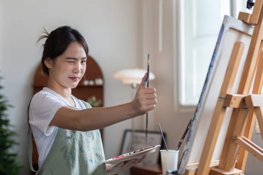 close up picture of happy young Asian woman painting brush on canvas in painting studio. In the art workshop class..