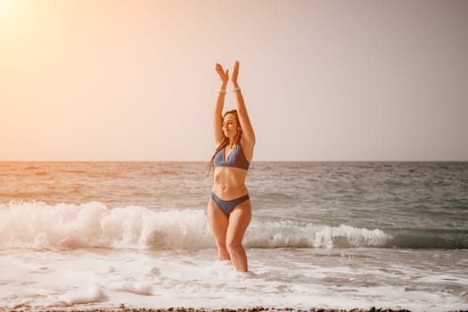 Beach vacation. Hot beautiful woman in sunhat and bikini standing with her arms raised to her head enjoying looking view of beach ocean on hot summer day.