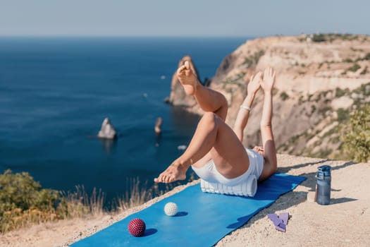 Middle aged well looking woman with black hair doing Pilates with the ring on the yoga mat near the sea on the pebble beach. Female fitness yoga concept. Healthy lifestyle, harmony and meditation.