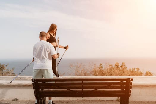 Happy Middle aged couple or friends practicing nordic walking in park near sea. Mature couple with trekking poles walking, practicing Nordic walking outdoors. Aging youthfully and sport concept.