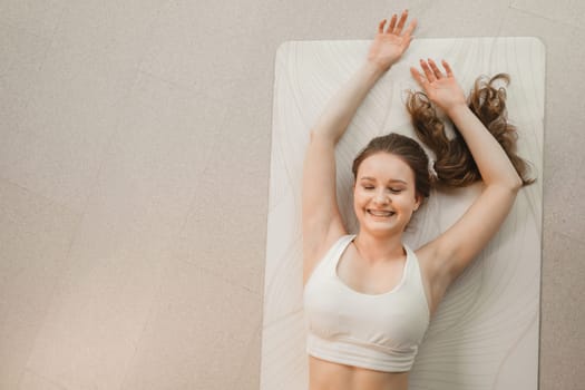 A girl in white clothes lies on a rug and laughs before yoga classes indoors.